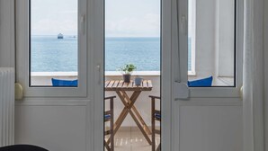 A room with a view of the sea through a glass door, a wooden table with a potted plant, and a black chair. - True Blue by halu! - Seafront 2BR apartment (Thessaloniki)