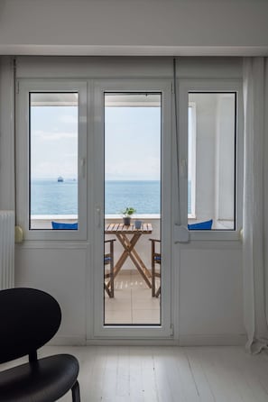 Ein Zimmer mit Meerblick durch eine Glastür, ein Holztisch mit einem Blumentopf und ein schwarzer Stuhl.