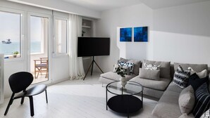A modern living room with a sofa, a coffee table, a TV on a stand, and a view of the sea through large windows. - True Blue by halu! - Seafront 2BR apartment (Thessaloniki)