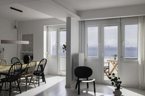 Ein Essbereich mit Tisch und Stühlen, einem Heizkörper und Blick auf das Meer durch große Fenster.