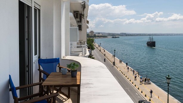 A balcony with a view of the sea, a table with chairs, and a potted plant. - True Blue by halu! - Seafront 2BR apartment (Thessaloniki)
