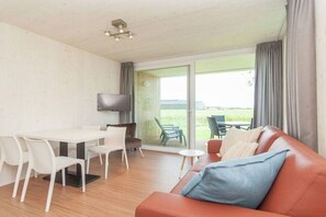 Ein Zimmer mit Esstisch, Stühlen, einer Couch, einem Fernseher und Blick durch eine Glastür.
