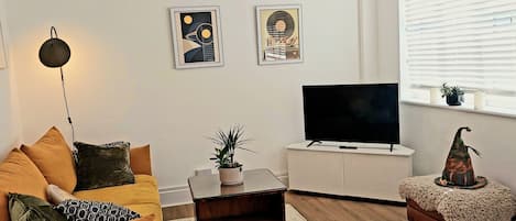 A living room with a sofa, a coffee table, a television, and a window with blinds.