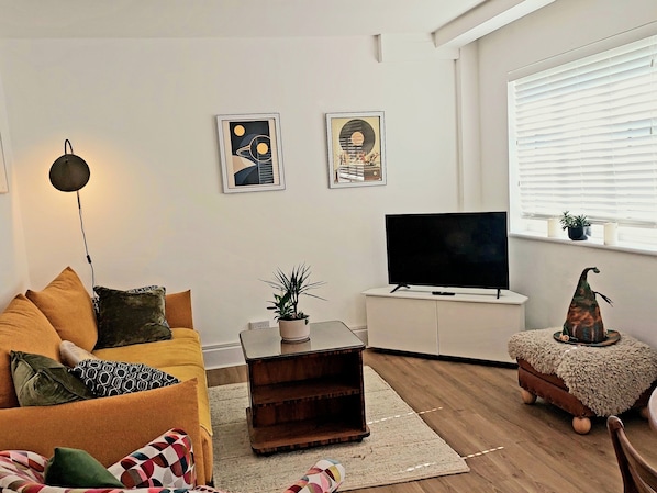 Una sala de estar con un sofá, una mesa de centro, un televisor y una ventana con persianas.