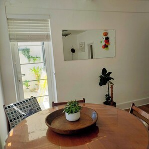 A dining area with a round wooden table, chairs, a potted plant, a mirror, and a view through a window. - Bournemouth Central +Free Parking. One Bed Modern Apartment. 8mins Beach (Bournemouth)