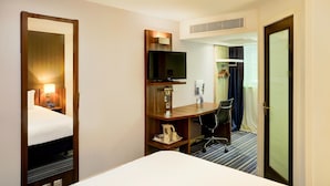 Een hotelkamer met een bed, bureau, stoel, televisie en een spiegel.