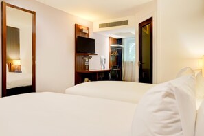 Quarto de hotel com cama, escrivaninha, cadeira, televisão e guarda-roupa.