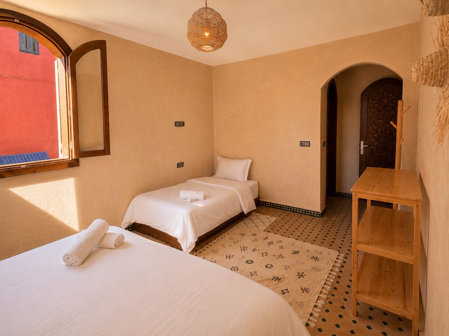 A hotel room with two beds, a wooden nightstand, a patterned rug, and a large window.