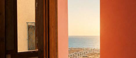 A room with a large window overlooking a beach and the ocean.