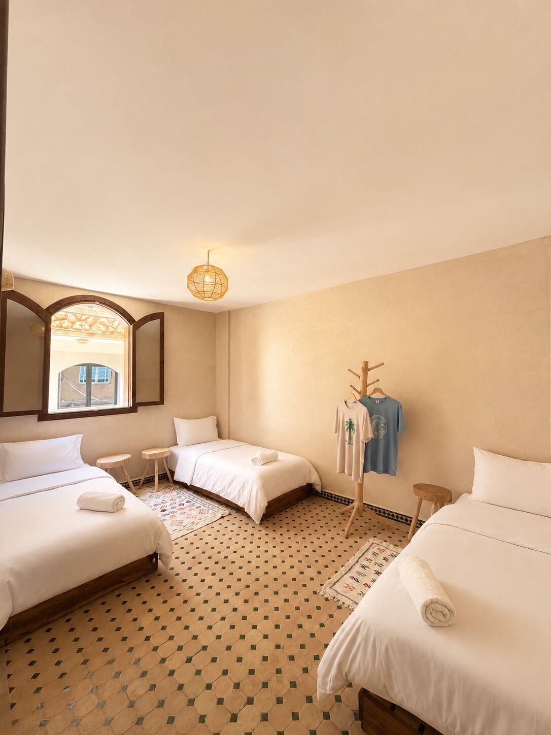 Habitación de hotel con dos camas, una mesita, una lámpara colgante y vistas por la ventana.