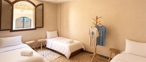 Habitación de hotel con dos camas, una mesita, una lámpara colgante y vistas por la ventana.