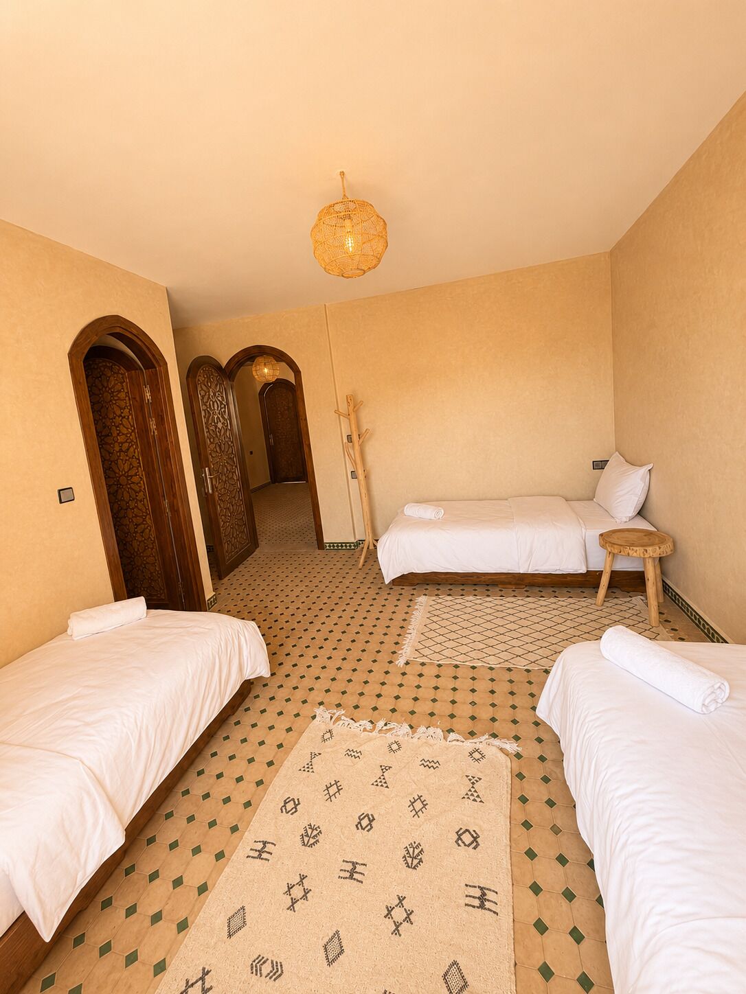 A hotel room with two single beds, a sitting area with a small table, a patterned rug, and a decorative hanging light fixture.
