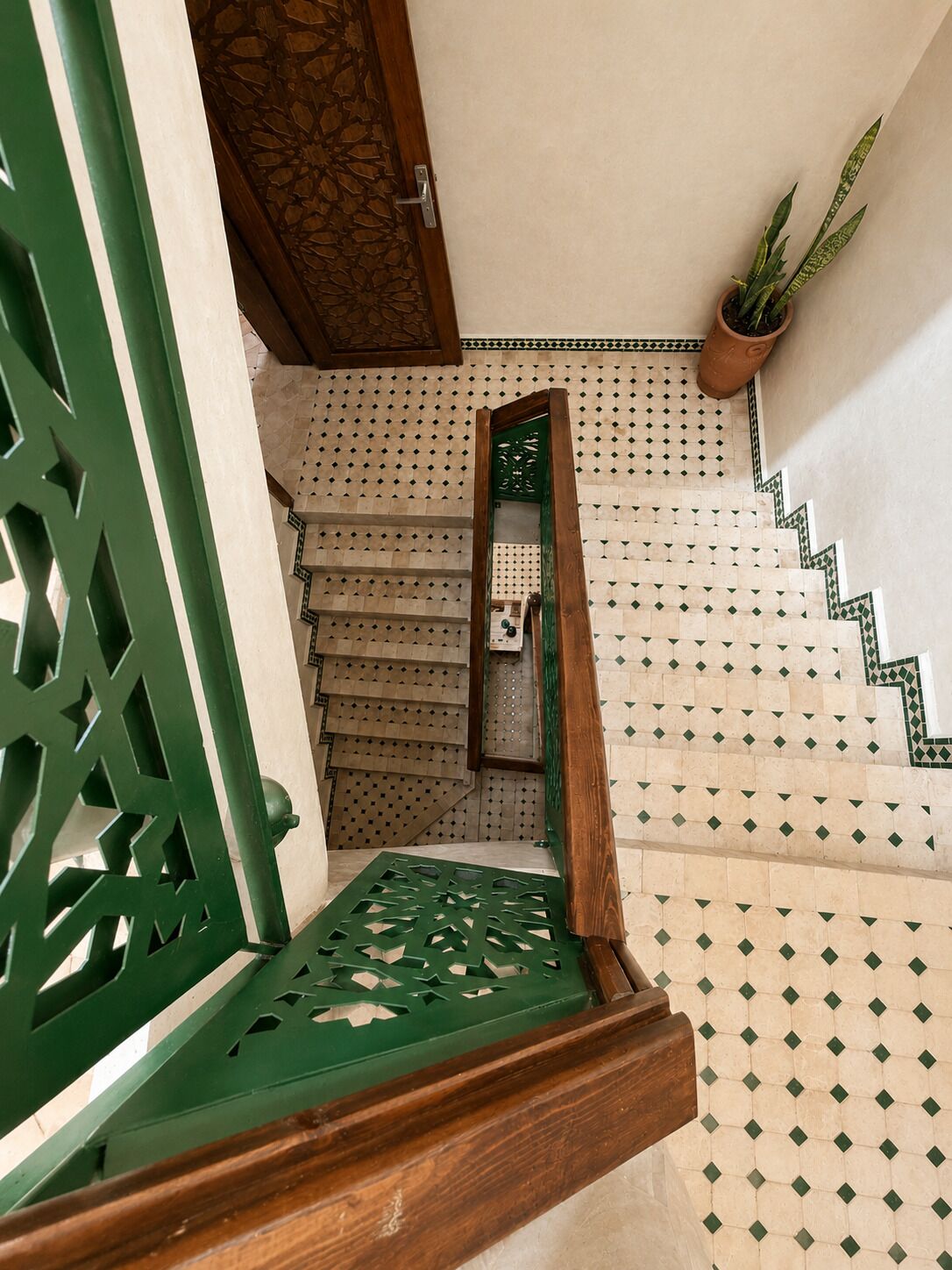 Una escalera con baldosas estampadas y barandilla de metal verde.