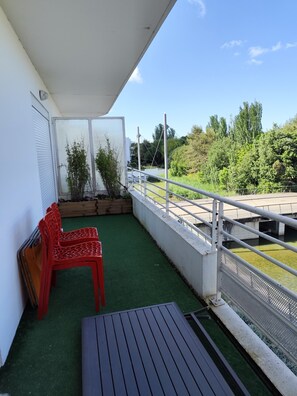 Ein Balkon mit künstlichem Rasen, einem Metalltisch und zwei roten Plastikstühlen.