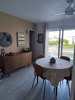 Ein Essbereich mit rundem Tisch und Korbstühlen, einem Holzschrank und einem großen Spiegel an der Wand.