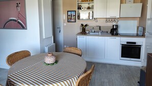 Ett kompakt kök med vita skåp, en inbyggd ugn och en matplats med ett randigt bordsduksöverdrag.