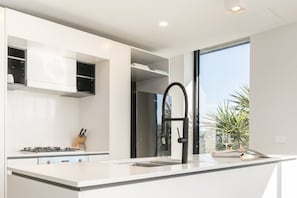A modern kitchen with white cabinetry, a stainless steel refrigerator, a black faucet, and a window providing a view of palm trees. - Sub-Penthouse with Lake Views | Kingston Foreshore (Kingston)