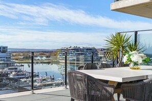 A balcony with a table, chairs, a vase with flowers, and a view of a marina and buildings across a body of water. - Sub-Penthouse with Lake Views | Kingston Foreshore (Kingston)