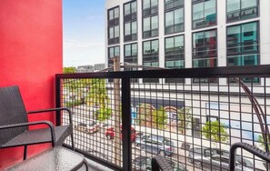 A balcony with a red wall, a metal railing, and a view of a parking lot and buildings. - Rooftop Pool · Heart of Wynwood · Modern Loft (Miami)