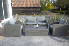 Eine Terrasse mit Korbmöbeln, darunter eine Couch und zwei Sessel, sowie ein kleiner Tisch.