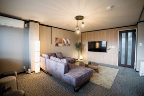 Ein modernes Wohnzimmer mit einer Couch, einem Flachbildfernseher, einer Pflanze und einer Deckenleuchte.