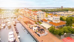 Una marina con barcos amarrados, una hilera de edificios con balcones y un estacionamiento.