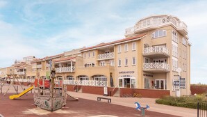 Un hotel con varios balcones, un parque infantil y una zona de arena.