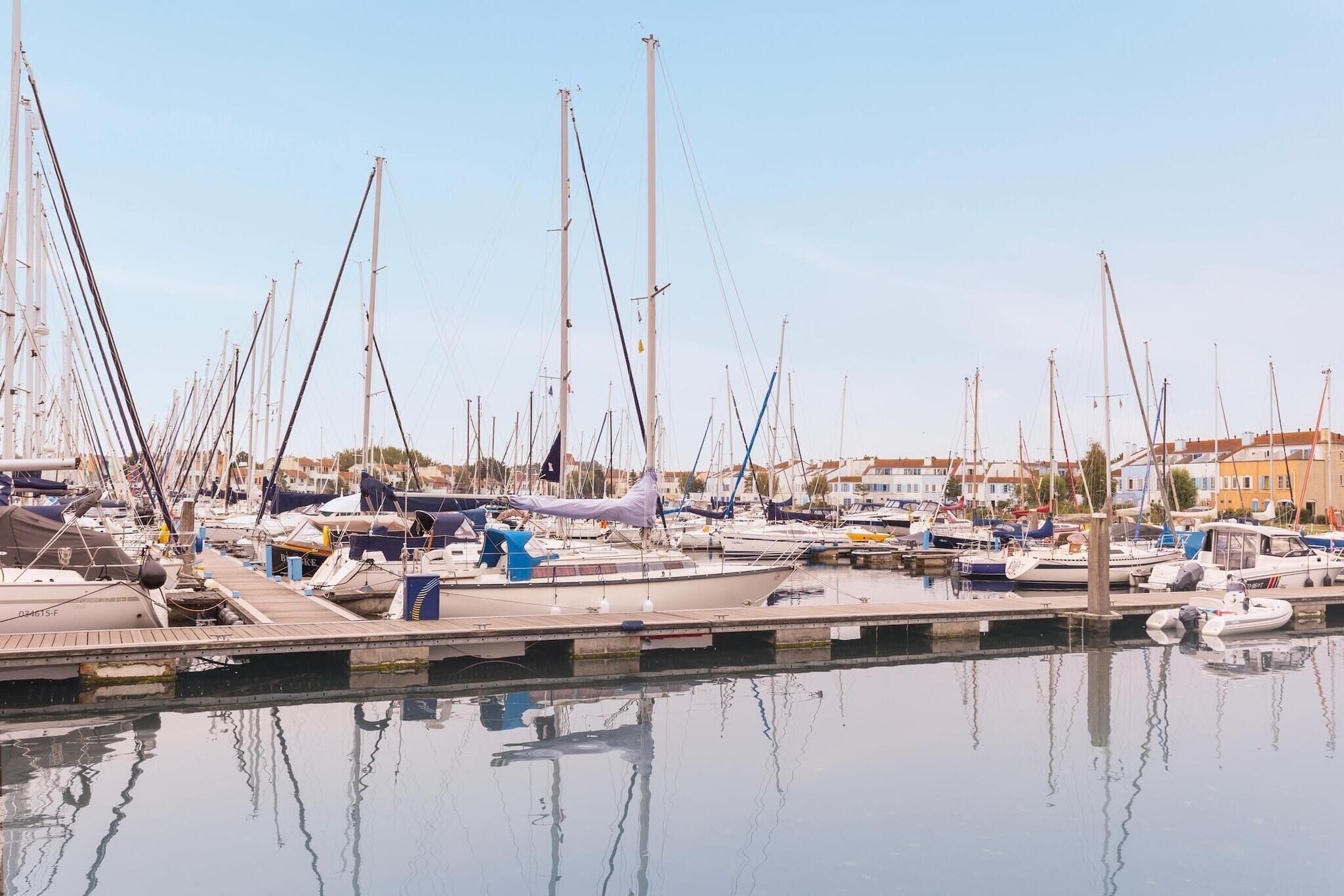 Een jachthaven met diverse boten aangemeerd aan steigers, kalm water en gebouwen op de achtergrond.