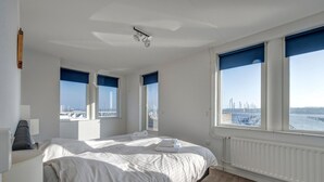 Un dormitorio con una cama grande, vista a un paisaje urbano y una ventana con vista a un puente.