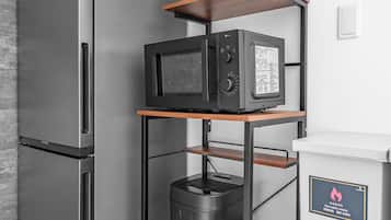 A kitchen with a stainless steel refrigerator, a microwave, a coffee maker, and a shelf unit with appliances.