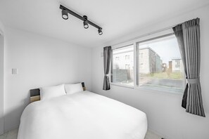 Un dormitorio con una cama grande, una ventana con cortinas, una lámpara en el techo y vistas a edificios.