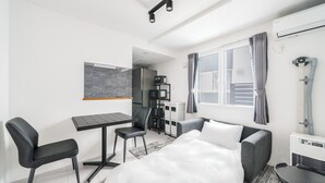 Habitación de hotel pequeña con cama, escritorio, silla, kitchenette y ventana con cortinas.