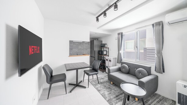 Una sala moderna con televisor de pantalla plana, un sofá, una mesa de centro y un comedor con mesa y sillas.