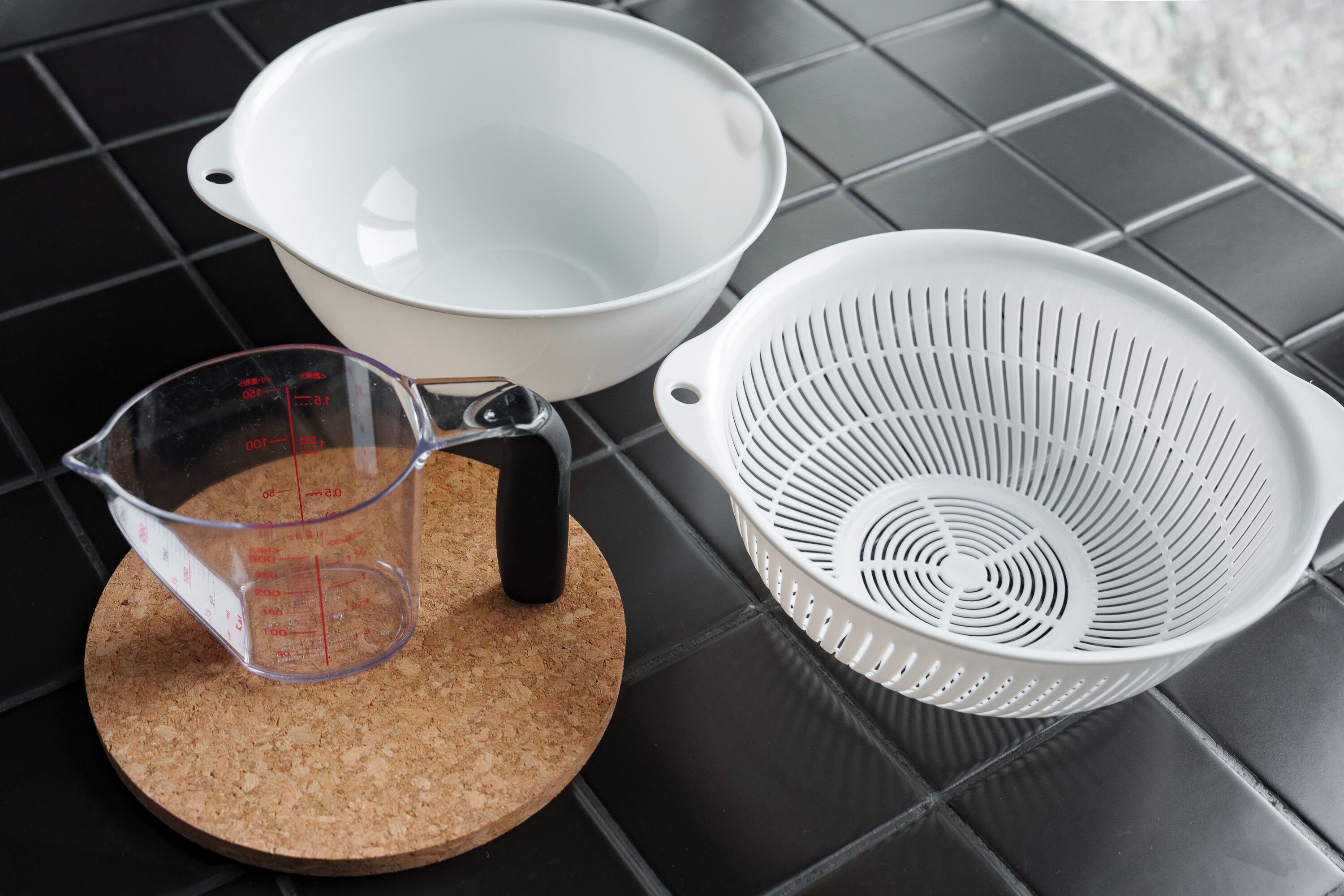 A kitchen counter with a measuring cup, a white bowl, and a colander.