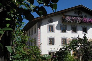 Ein traditionelles Gebäude mit einem Balkon, der mit Blumen geschmückt ist, bewölkter Himmel und umgebender Bepflanzung.