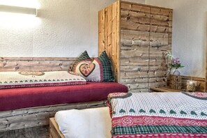 Ein Zimmer mit Holz-Kopfteil, zwei Betten mit gemusterten Bettbezügen, einem Nachttisch mit einer Vase und einem Holzschrank.