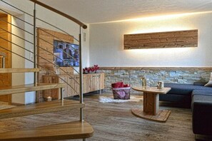 Ein modernes Interieur mit einer Holztreppe, einer Steinwand, einem blauen Sofa und einem kleinen runden Tisch.