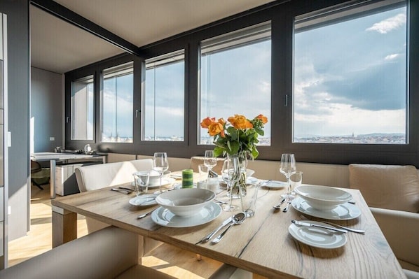 A dining area with a table set for four, large windows, and a city view. - Skyflats Vienna Black View (Wien)