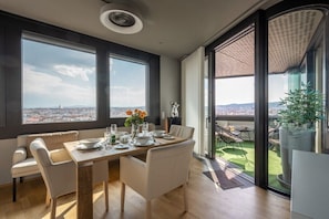 A dining area with a table set for four, large windows, and a balcony with a view. - Skyflats Vienna Black View (Wien)