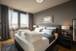 A hotel room with a large bed, two bedside tables, a nightstand, a window with curtains, and a view of the city. - Skyflats Vienna Black View (Wien)