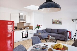 Eine moderne Küche mit weißen Schränken, einem roten Kühlschrank und einem grauen Sofa im Wohnbereich.