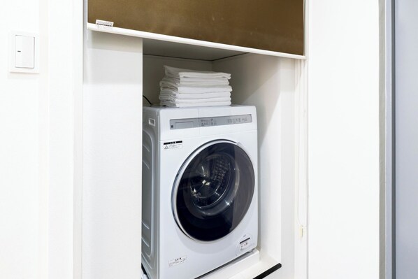 A white washing machine in a white cabinet with a shelf above it holding folded clothes. - Opening in 2026 1 minute walk from Tojinmachi St / Fukuoka City Fukuoka (Fukuoka City)