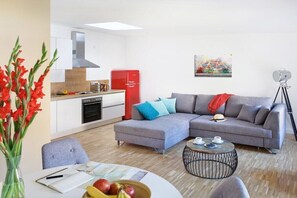 A modern living room with a grey sofa, a small round coffee table, and a dining area with a white table and a vase of red flowers. - Holiday apartment in Potsdam with Wi-Fi (Potsdam)