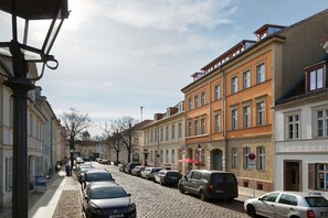 Eine Kopfsteinpflasterstraße gesäumt von historischen Gebäuden, parkenden Autos und einem klaren Himmel.