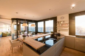 A modern kitchen with a central island, pendant lights, and a view of the city. - Skyflats Vienna Hills View (Wien)