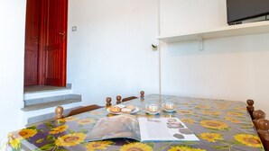 Ein Essbereich mit einem für zwei Personen gedeckten Tisch, einer roten Tür und einem an der Wand befestigten Fernseher.