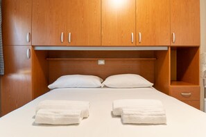 Ein Hotelzimmer mit Holzschrank, einem Bett mit weißer Bettwäsche und zwei Handtüchern auf dem Bett.
