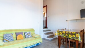 Ein Wohnzimmer mit einer Couch, einem Esstisch mit Stühlen, einer Treppe und einem Fernseher an der Wand.