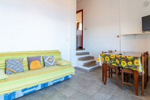 Ein Wohnzimmer mit einer Couch, einem Esstisch mit Stühlen, einer Treppe und einem Fernseher an der Wand.