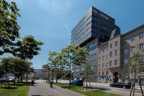Ein modernes Mehrgeschosshaus mit befestigtem Gehweg und einem begrünten Bereich mit Bäumen.